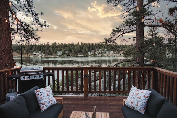 Una terraza con una parrilla, dos sofás con cojines estampados y vistas a un lago y un bosque.
