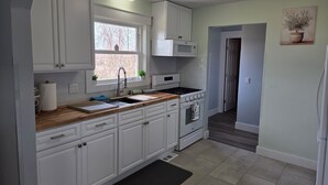 A kitchen with white cabinets, a stove, a sink, and a window.