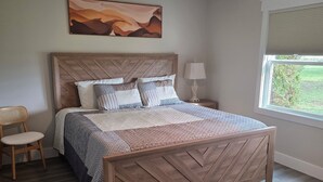 A bedroom with a wooden bed, a ceiling fan, a nightstand with a lamp, a chair, and a window with a view.