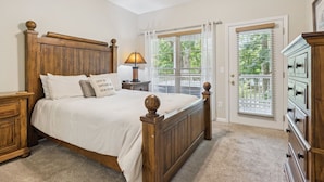 A bedroom with a wooden bed, a nightstand, a lamp, a dresser, and a view of the outdoors through a window. - Welcome to Ritz on the River, your peaceful Smoky Mountain retreat! (Pigeon Forge)