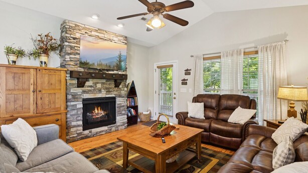 A living room with a stone fireplace, leather sofa, and a ceiling fan. - Welcome to Ritz on the River, your peaceful Smoky Mountain retreat! (Pigeon Forge)