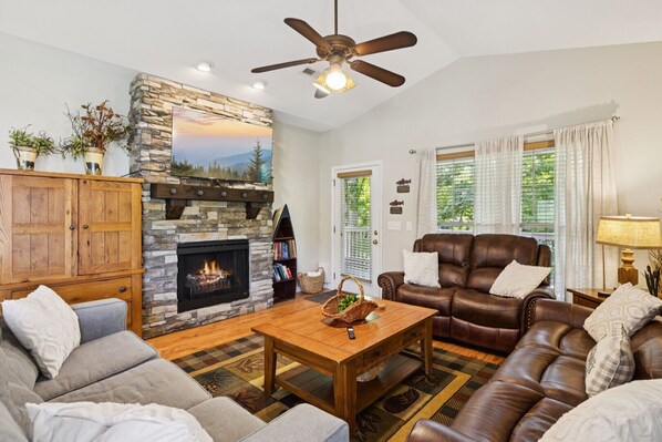 A living room with a stone fireplace, leather sofa, and a ceiling fan. - Welcome to Ritz on the River, your peaceful Smoky Mountain retreat! (Pigeon Forge)