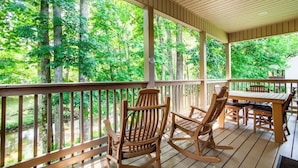 A wooden deck with rocking chairs and a table, overlooking a forested area. - Welcome to Ritz on the River, your peaceful Smoky Mountain retreat! (Pigeon Forge)