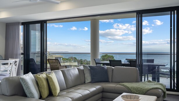 Ein modernes Wohnzimmer mit einem großen Schiebeglastür, die auf einen Balkon mit Meerblick führt.