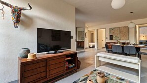 A modern living room with a flat-screen TV, wooden entertainment unit, and a dining area with a white bench and chairs. - Quiet and Cozy Home with Great Location (Queretaro)