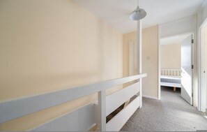 A hallway with a white railing, a ceiling light, and an open door leading to a room with a bed. - 4-Bed Maisonette with Balcony (Greater London)