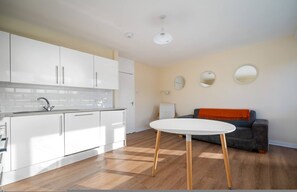 A modern kitchen with white cabinets, a white countertop, and a round table with wooden legs. - 4-Bed Maisonette with Balcony (Greater London)