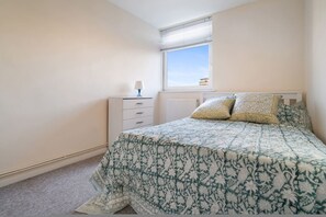 Ein Schlafzimmer mit Bett, Nachttisch, Lampe und einem Fenster mit Jalousien.