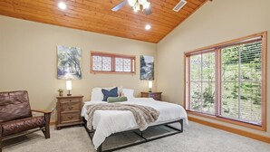 Une chambre à coucher avec un lit, un plafond en bois, une fenêtre avec des stores et des œuvres d’art accrochées aux murs.