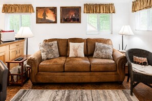 Eine braune Ledersofa mit gemusterten Kissen, ein Holztisch, ein Korbstuhl und ein Teppich.