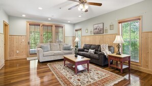 A living room with wooden flooring, a ceiling fan, two sofas, a coffee table, and large windows with blinds. - Serenity Ridge 313 - King Bed/Clubhouse Access (Pigeon Forge)