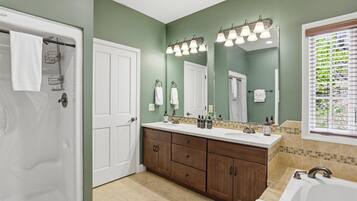 A bathroom with a shower, a double sink vanity, a large mirror, and a window with blinds.
