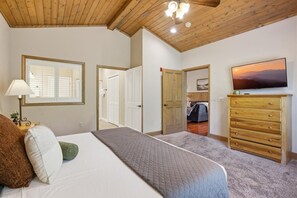 Un dormitorio con cama, cómoda, televisor y puerta que da a otra habitación.