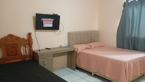 Een slaapkamer met twee bedden, een bureau, een aan de muur bevestigde televisie en een gordijn voor het raam.