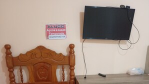 Een slaapkamer met een houten bed, een bureau met lades, een televisie aan de muur en een bord boven het bed.