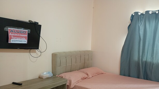 Een slaapkamer met een bed, een bureau, een aan de muur bevestigde televisie en een gordijn.