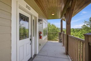 A covered porch with a fire extinguisher, a number '323' on the door, and a view of greenery. - Serenity Ridge 323- Clubhouse Access/King Bed/WiFi (Pigeon Forge)