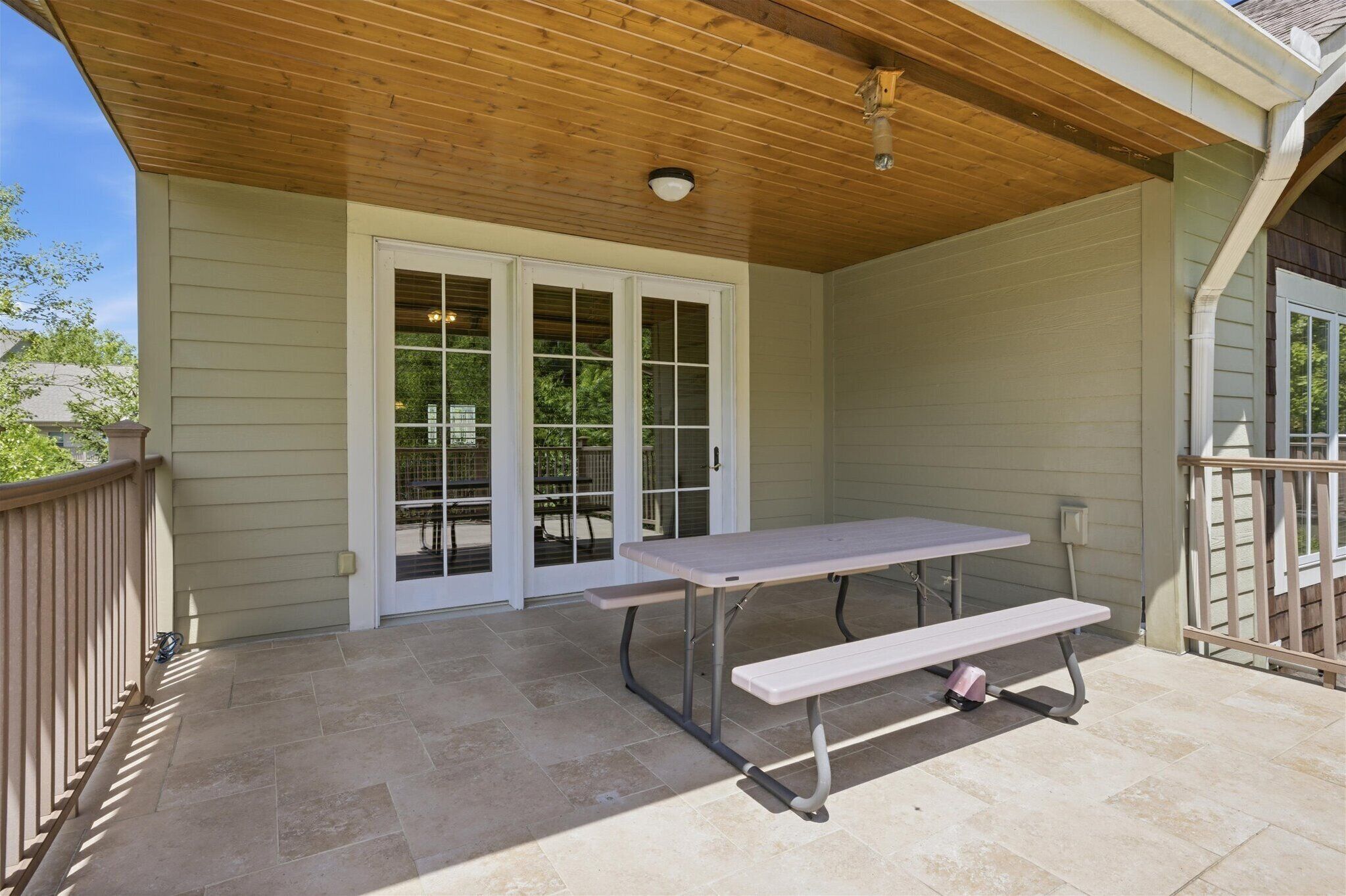 Un patio couvert avec une table de pique-nique et un banc, une porte-fenêtre coulissante et un plafond en bois.