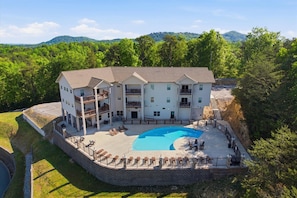 A multi-story building with a swimming pool, outdoor seating, and a mountainous backdrop.