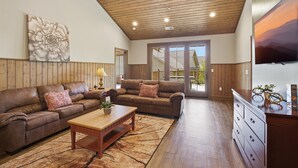 A spacious living room with a wooden ceiling, two couches, a coffee table, a TV, and a large window. - Serenity Ridge Unit 721 - Groups/Pool Access/Patio (Pigeon Forge)