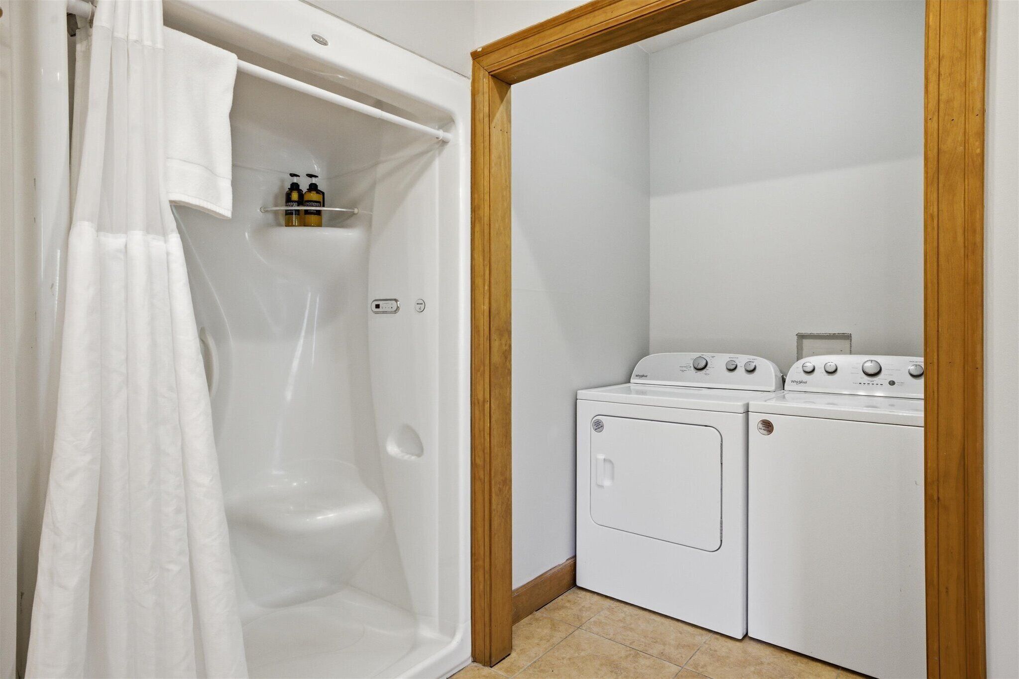 A laundry room with a white bathtub, two white washing machines, and a wooden door frame.