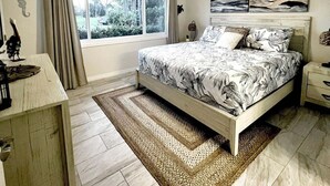 Een slaapkamer met een bed, een plafondventilator, een raam met gordijnen, een nachtkastje en een wandairconditioner.