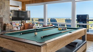 Mesa de bilhar com vista para a praia, televisão e área de estar com cadeiras.