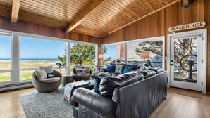 Interior de uma casa de praia com um amplo sofá de couro, cadeiras de vime e vista para o oceano.