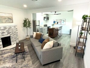 Uma sala de estar moderna com lareira, um sofá, uma mesa de centro e um espaço de refeições, com uma cozinha ao fundo.