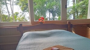 A bed with a quilted cover, a window with a view of trees, and a small vase with flowers on the windowsill.