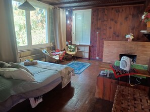 Una habitación con cama, una mesa con sillas, chimenea y una ventana con cortinas.