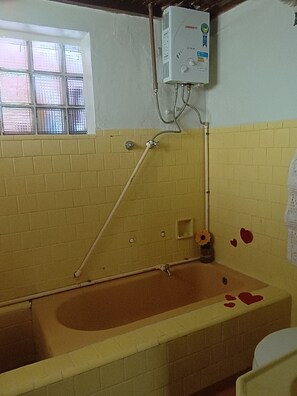Un baño con bañera, ventana y calentador de agua.