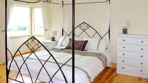 Una cama con dosel de cuatro postes, un aparador blanco con cajones y una ventana con cortinas.