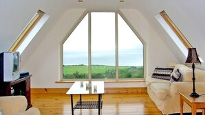 Dormitorio tipo loft con un tragaluz grande, un sofá blanco, una mesita y un televisor.