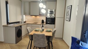 Et kompakt køkken med indbygget ovn, vaskemaskine samt spiseområde med fire stole og et bord.
