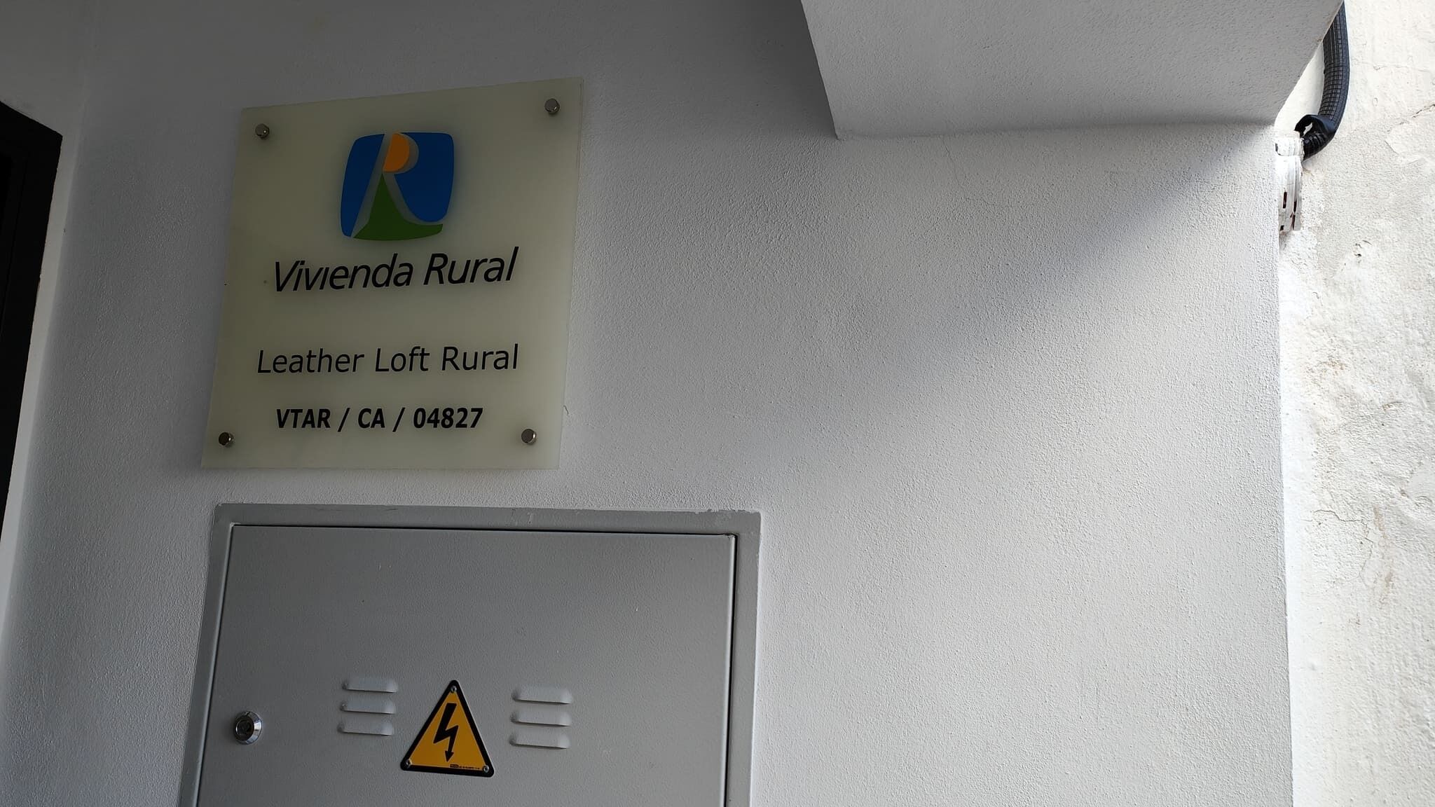 Un letrero que dice 'Vivenda Rural Leather Loft Rural' con un símbolo de peligro de rayos debajo.