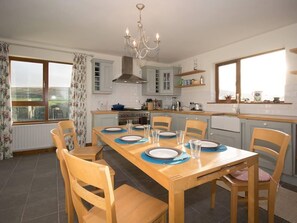 A kitchen with a dining table set for six, a chandelier, and a view through a window.