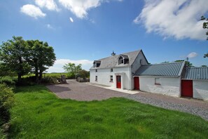 A white building with red doors, a gravel driveway, and a grassy area.