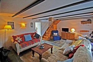 A cozy living room with a sofa, armchair, and a wooden staircase.
