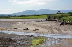 A coastal landscape with a dirt path, rocky shore, and a house in the background.