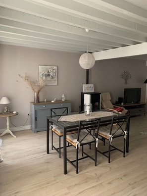 Un comedor con una mesa de vidrio, sillas negras, un mueble azul y una lámpara colgante.