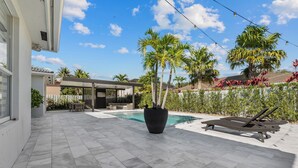 Ein moderner Poolbereich im Freien mit einer gefliesten Terrasse, Liegestühlen und einem großen Kübel mit Palmen.