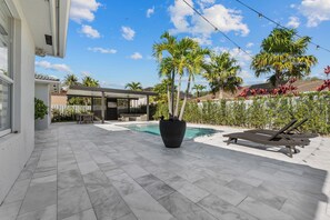 A modern outdoor pool area with a tiled patio, lounge chairs, and a large planter with palm trees.