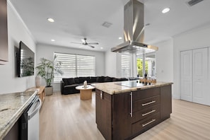 Una cocina moderna con una isla central, armarios de madera, un ventilador de techo y un comedor con sofá y mesa de centro.