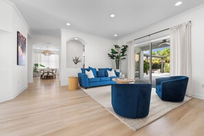 A modern living room with a blue sofa, a round coffee table, and a large window with curtains.