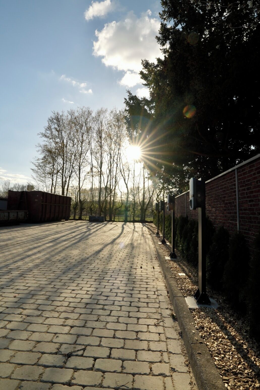 Un chemin pavé mène à un bâtiment dont le mur est en briques et qui est entouré d’une clôture en métal.