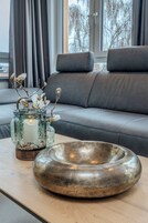 Una sala moderna con un sofá, un florero de vidrio con una vela, y un cuenco decorativo sobre una mesa de madera.