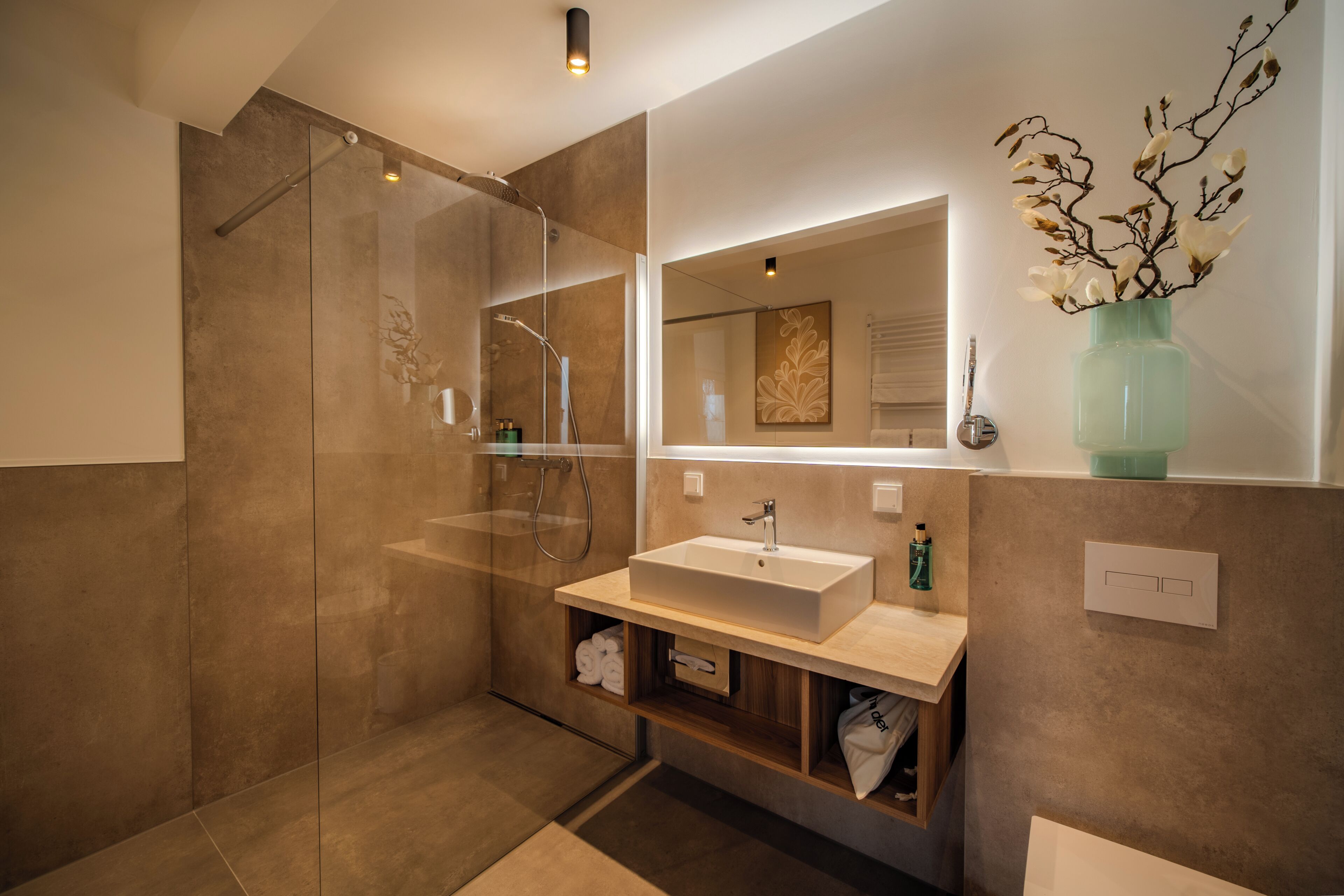 Une salle de bain moderne avec une douche à parois de verre, un grand miroir, un lavabo et un vase décoré de branches.