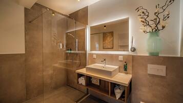 Une salle de bain moderne avec une douche à parois de verre, un grand miroir, un lavabo et un vase décoré de branches.