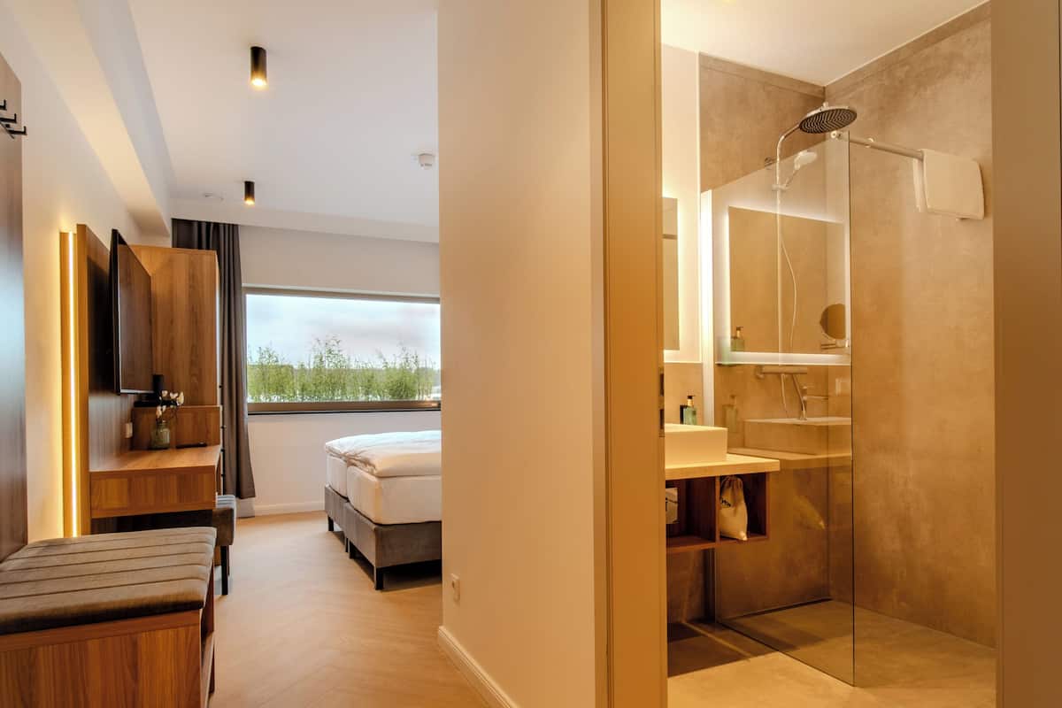 Una habitación de hotel moderna con suelo de madera, una cama, ducha, televisión y vistas al exterior.